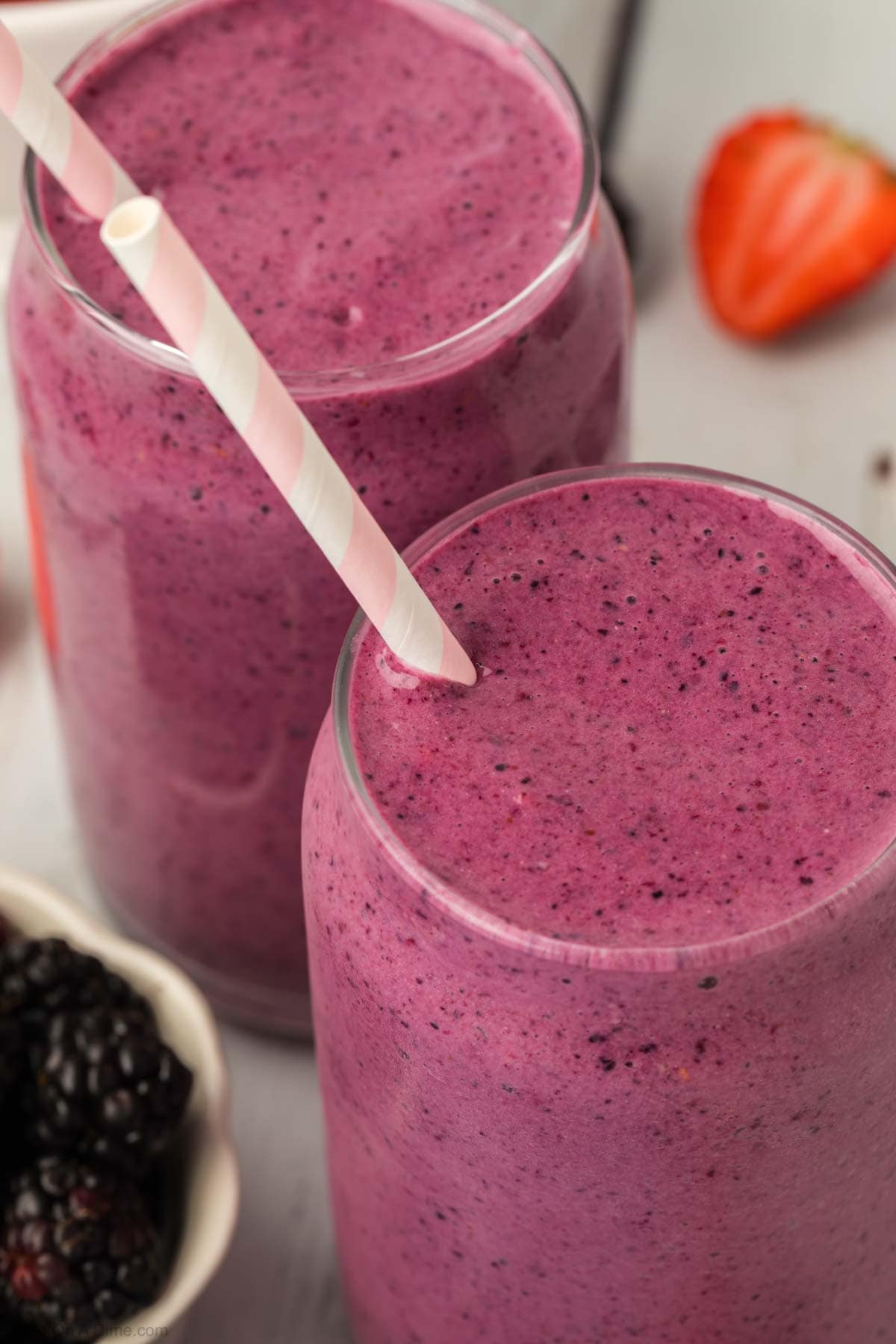 Mixed berries smoothie in a clear glass with a straw