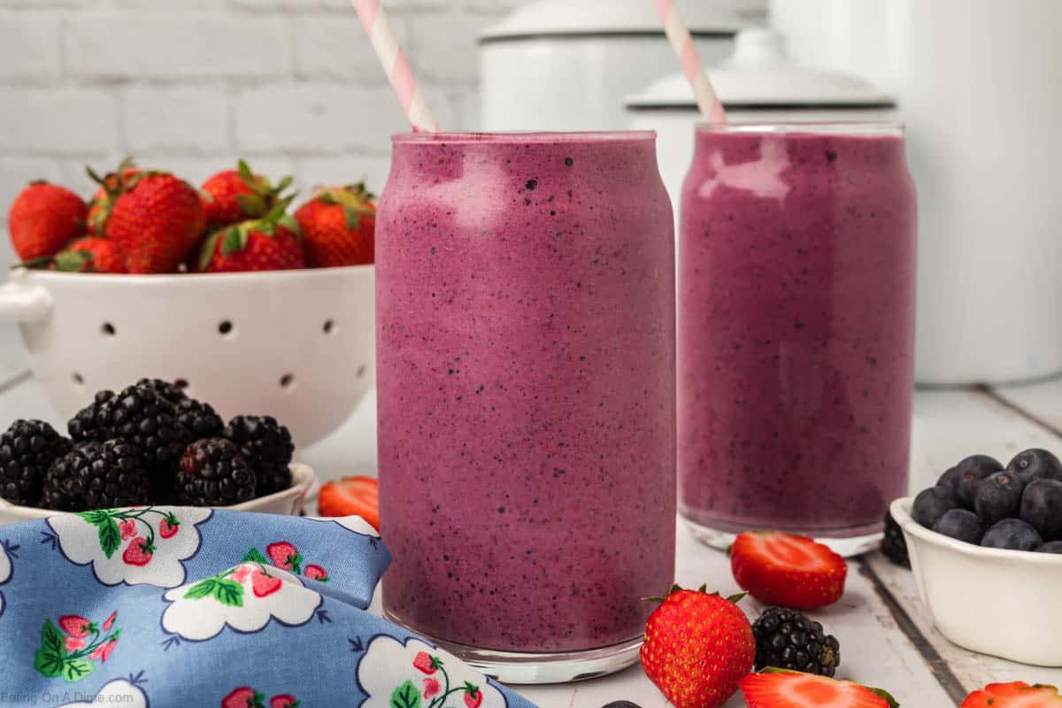 2 glasses of Fruit Smoothies with bowls of fresh fruit on the side.