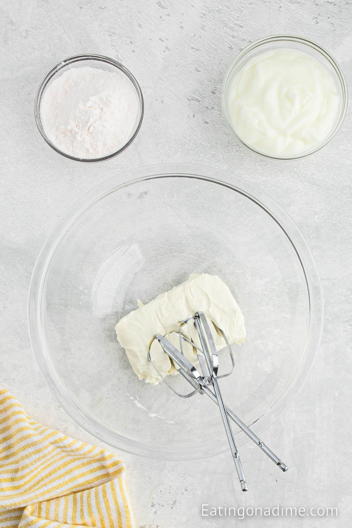 Beating cream cheese in a bowl with yogurt and pudding mix on the side