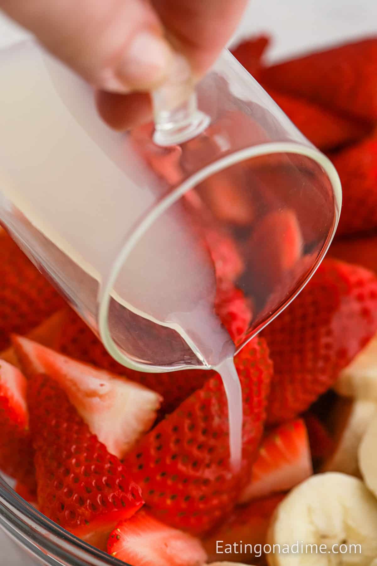 Pouring lemon juice over the fresh strawberries and bananas in the bowl