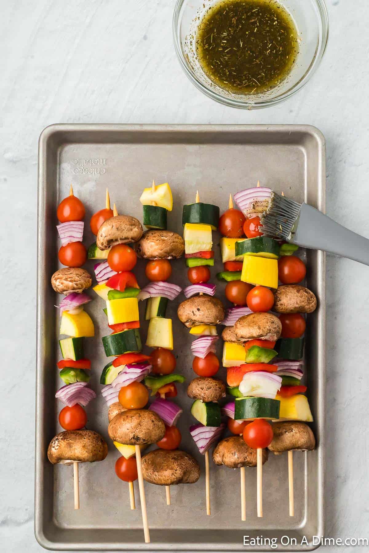 Vegetable kabobs on a baking sheet brushing with marinade on the kabobs