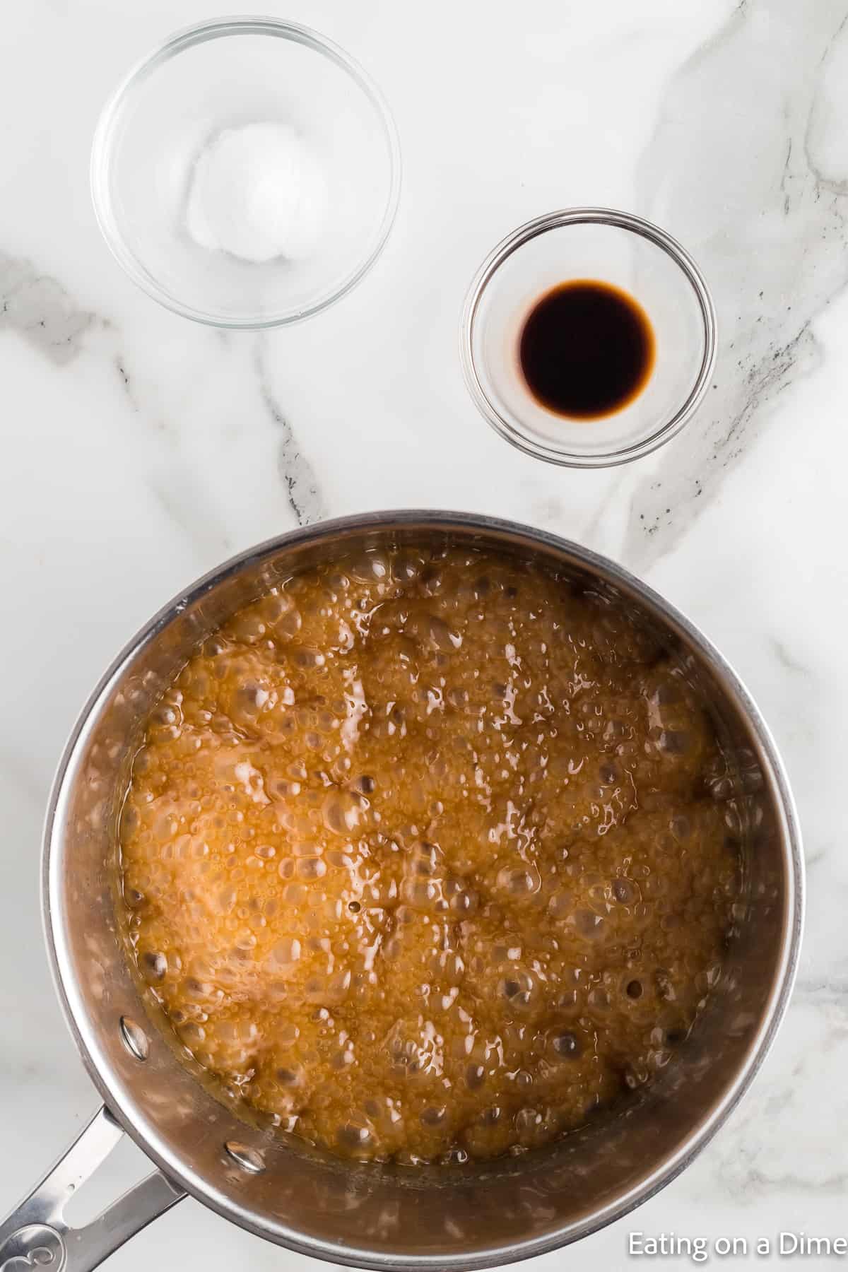 Brown sugar mixture boiling in a saucepan with bowls of vanilla and salt on the side