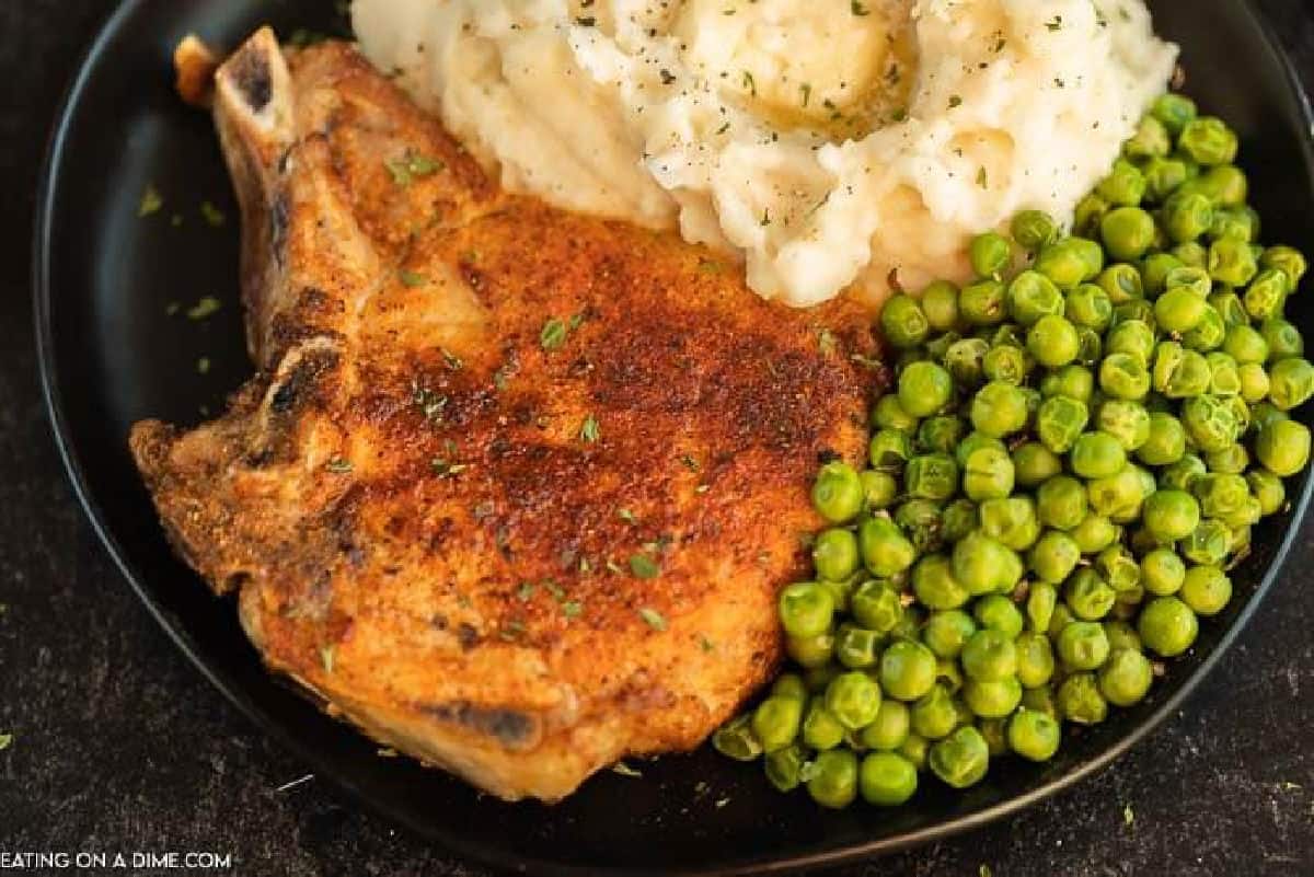 Bone In Pork Chops on a plate with peas and mashed potatoes