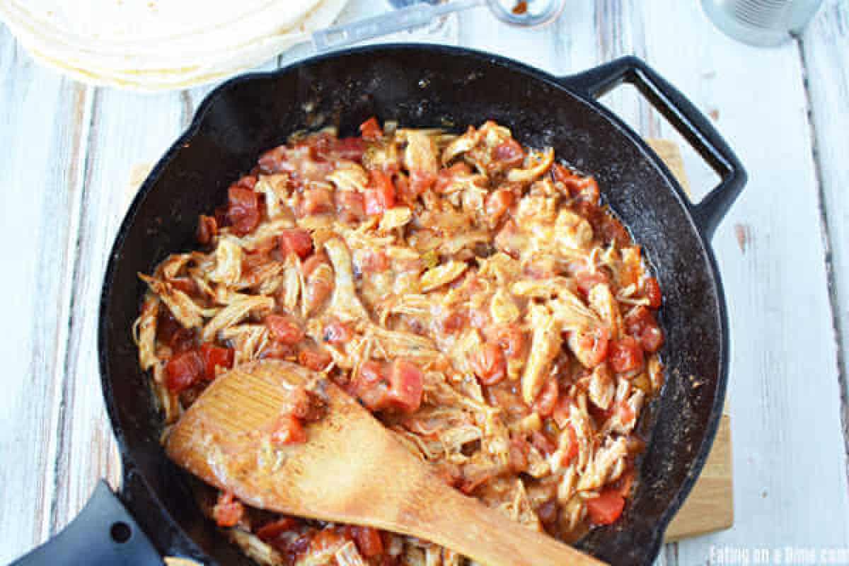 Mixing the cooked shredded chicken, rotel and cream of chicken soup in a cast iron skillet with a wooden spoon