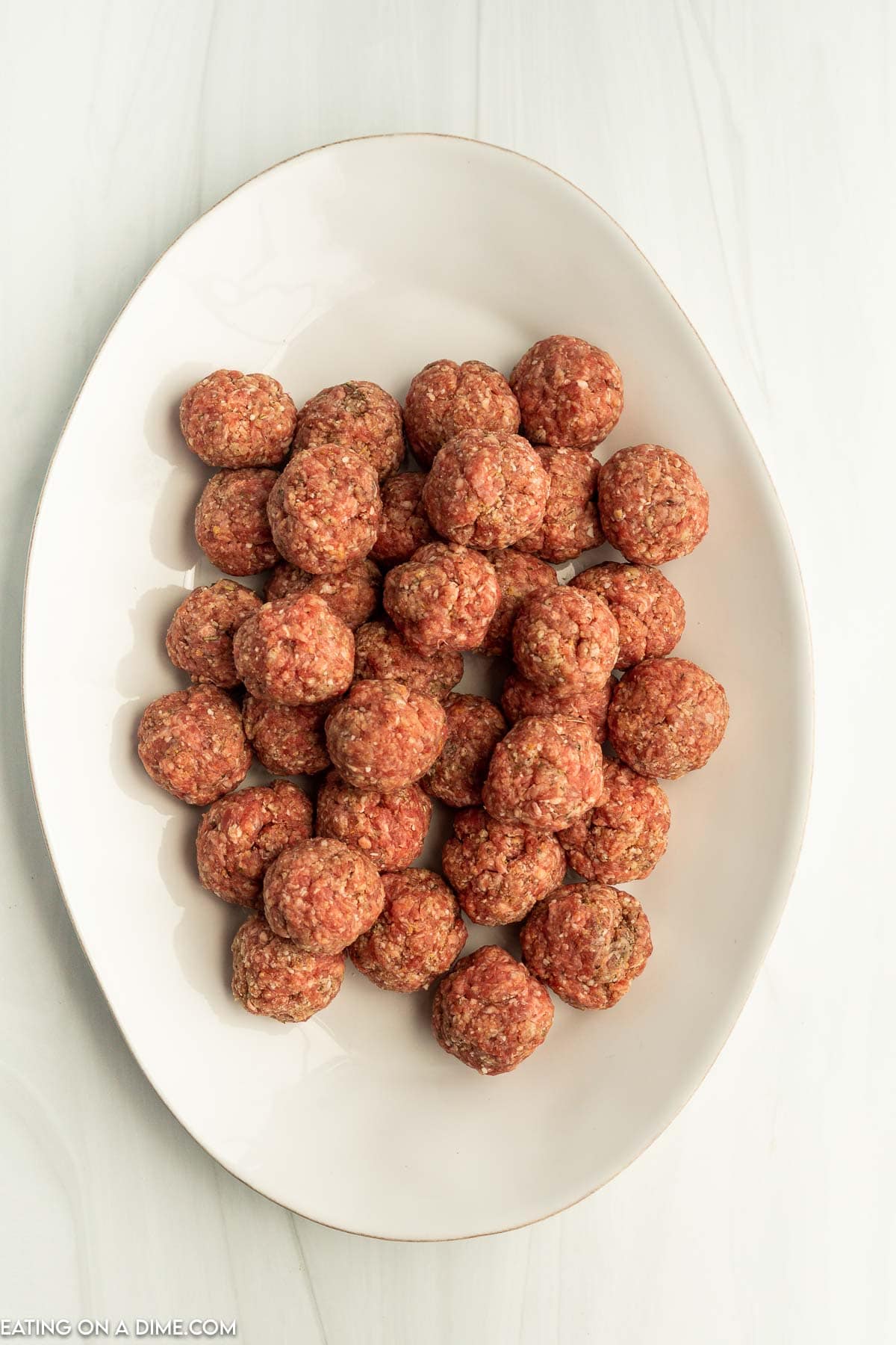 Uncooked meatballs stacked on a white platter