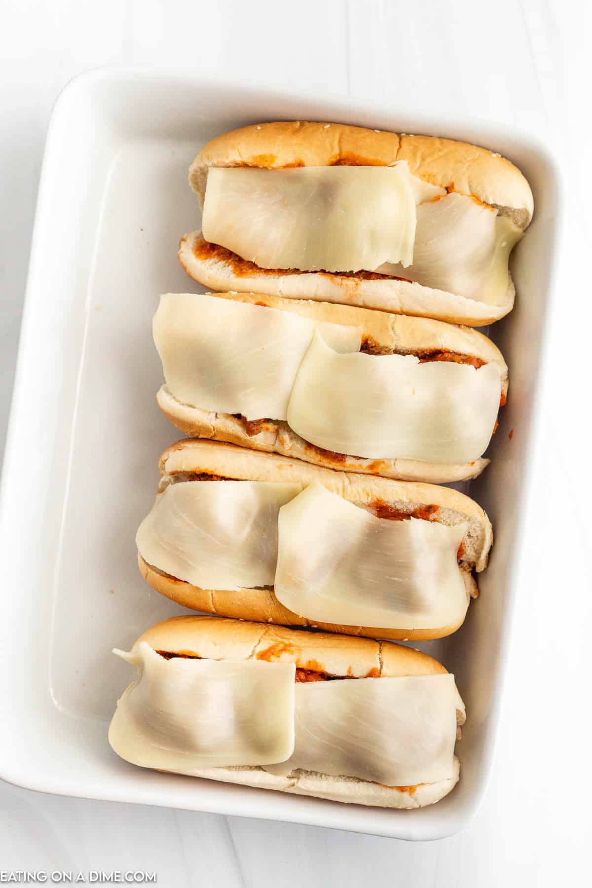 Meatball subs topped with slices of cheese in a baking dish