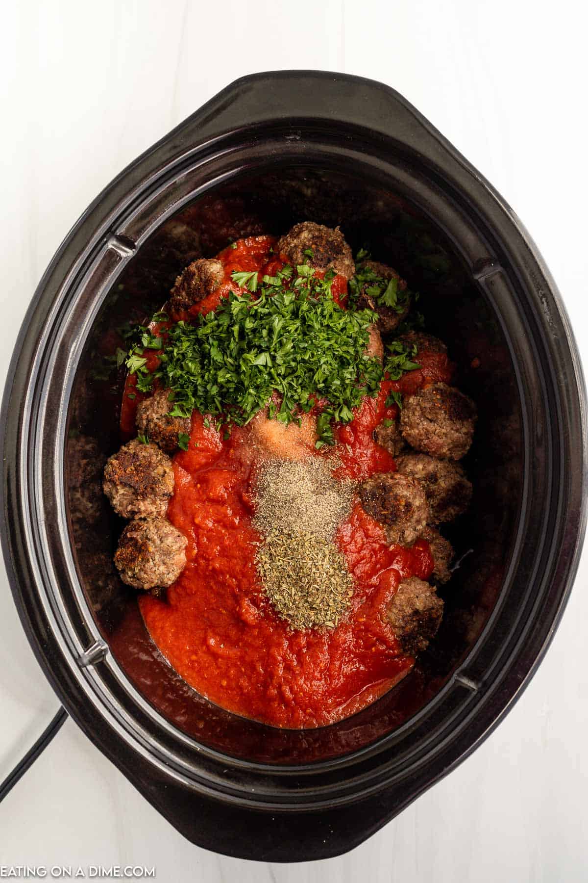 Topping the cooked meatballs with tomatoes, Italian Seasoning, salt, pepper, fresh parsley