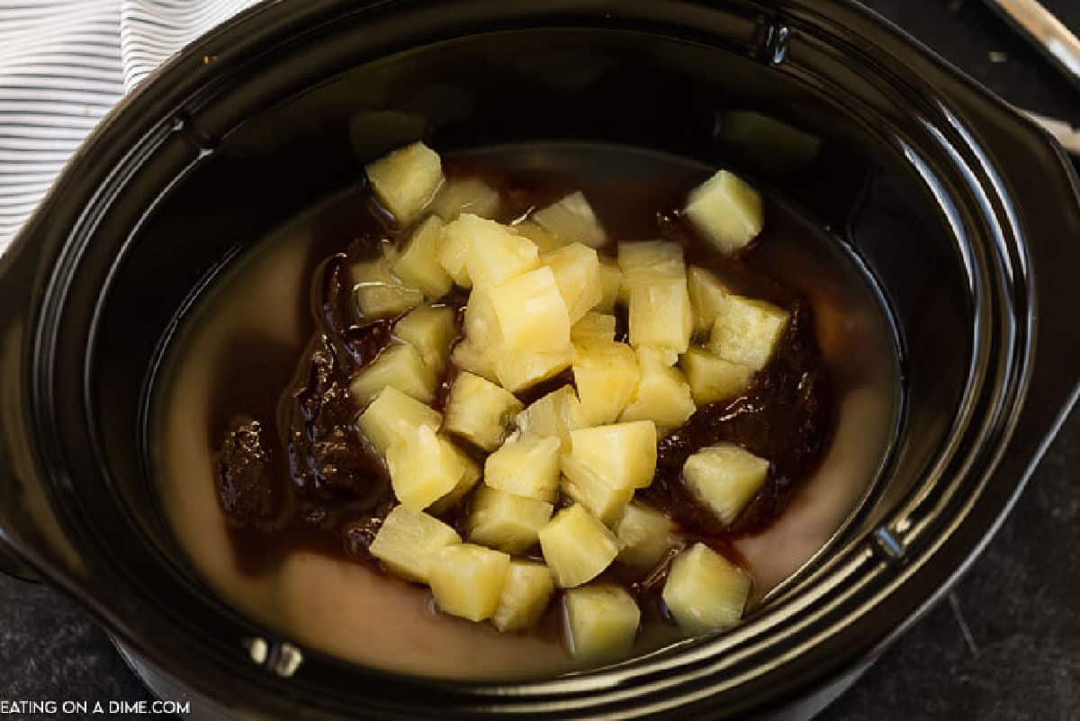 Uncooked chicken breast in the slow cooker topped with BBQ Sauce and chunks of pineapple