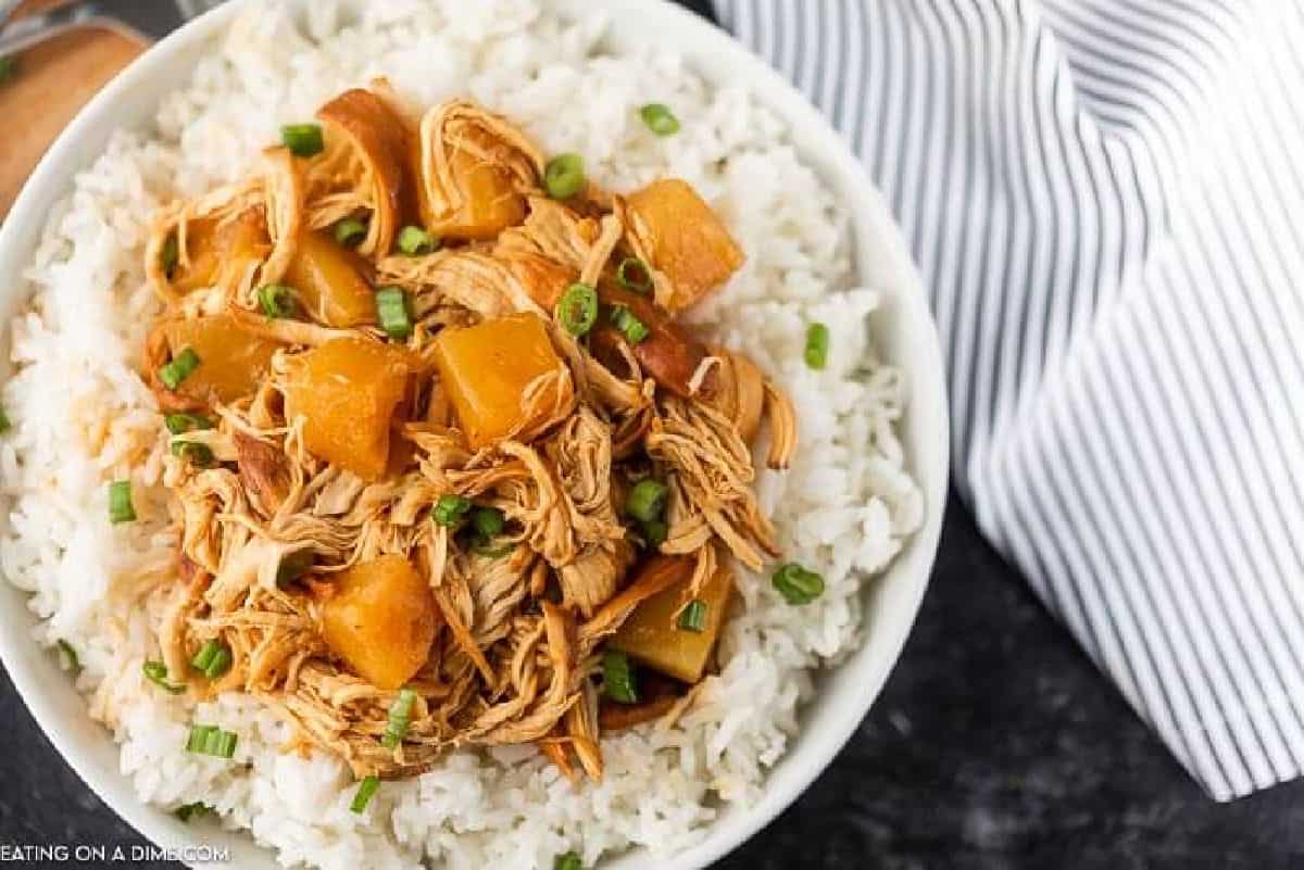 Hawaiian BBQ Chicken over Rice in a white bowl on a black countertop with a striped linen next to it 