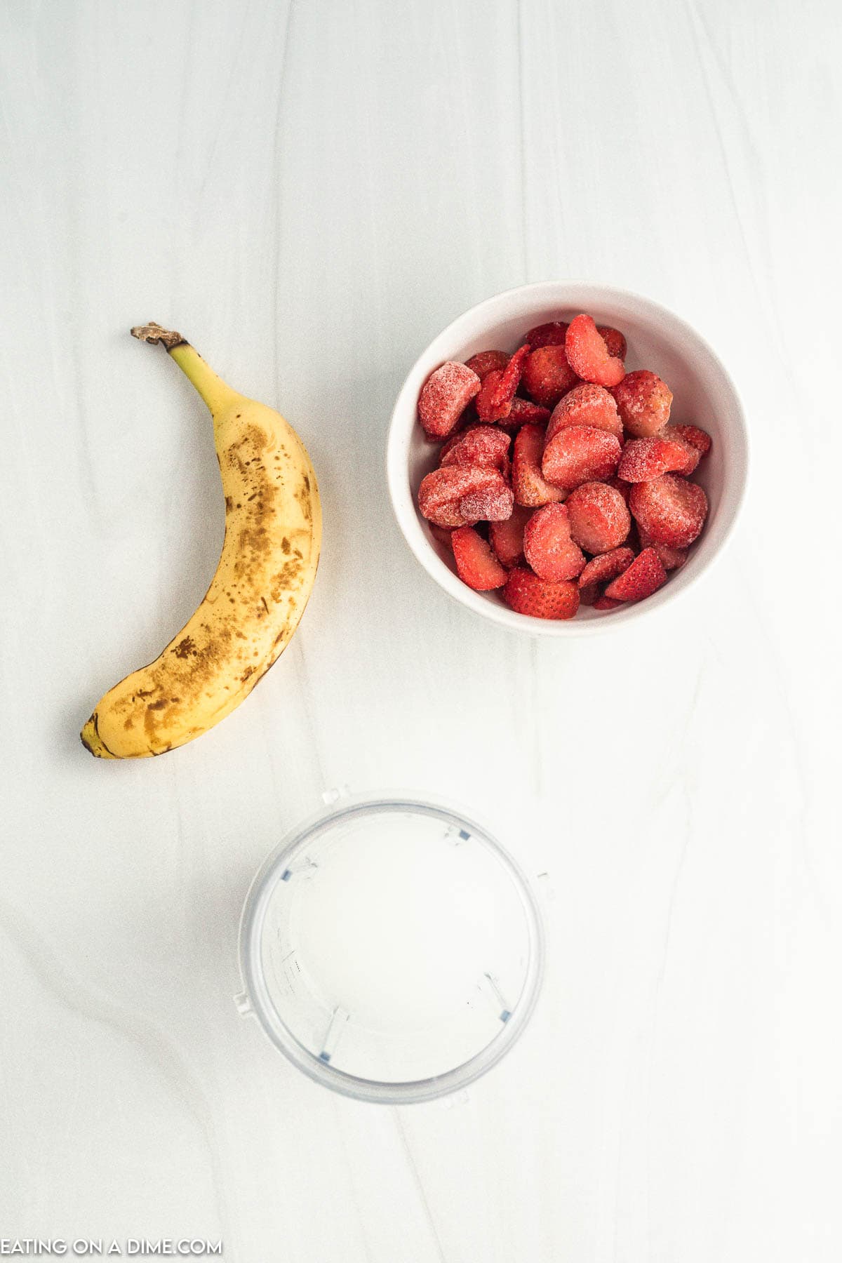 Placing milk in the blender cup with a bowl of frozen strawberries and a banana