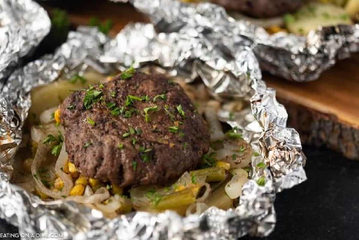 Hamburger patty in a foil packet with corn, slice onions and potatoes