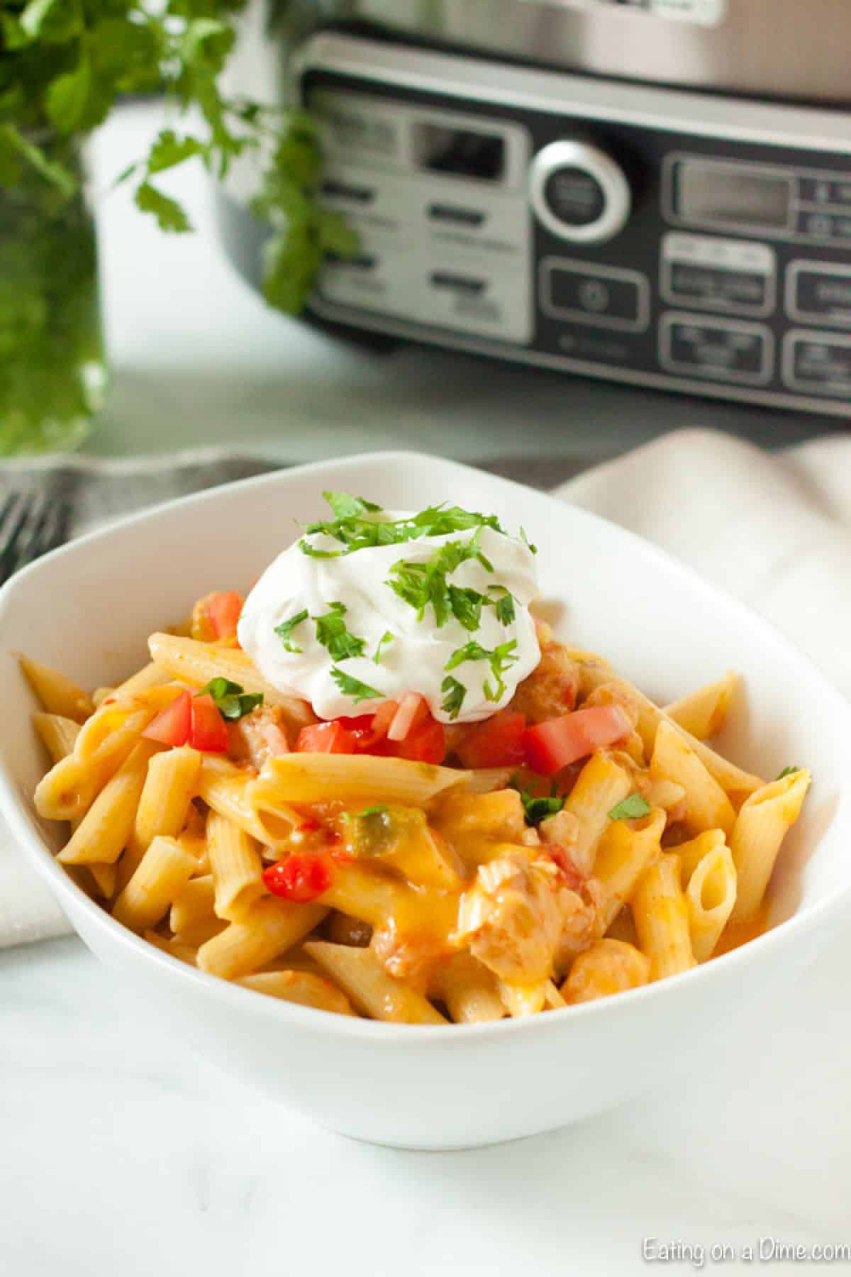 Chicken fajita pasta in a bowl topped with sour cream and diced tomatoes