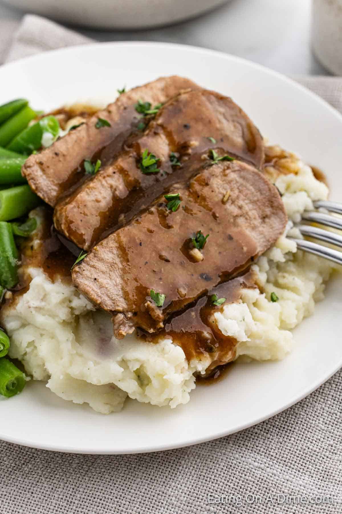 Slice pork tenderloin topped with a glaze over mashed potatoes and green beans on a plate