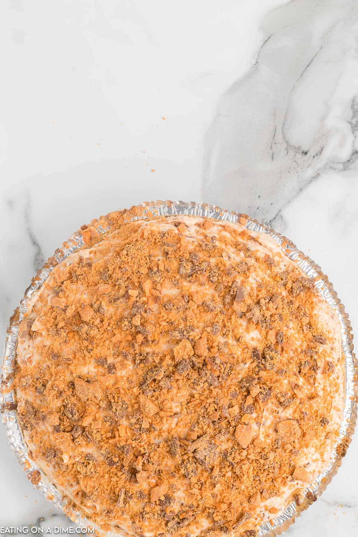 Spreading the peanut butter mixture into pie pan and topping with crushed butterfinger candy bars