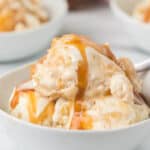 A close-up of vanilla ice cream in a white bowl, topped with a generous drizzle of caramel sauce—perfect inspiration for your next Caramel Apple Ice Cream Recipe. A spoon is partially visible on the right side of the bowl.