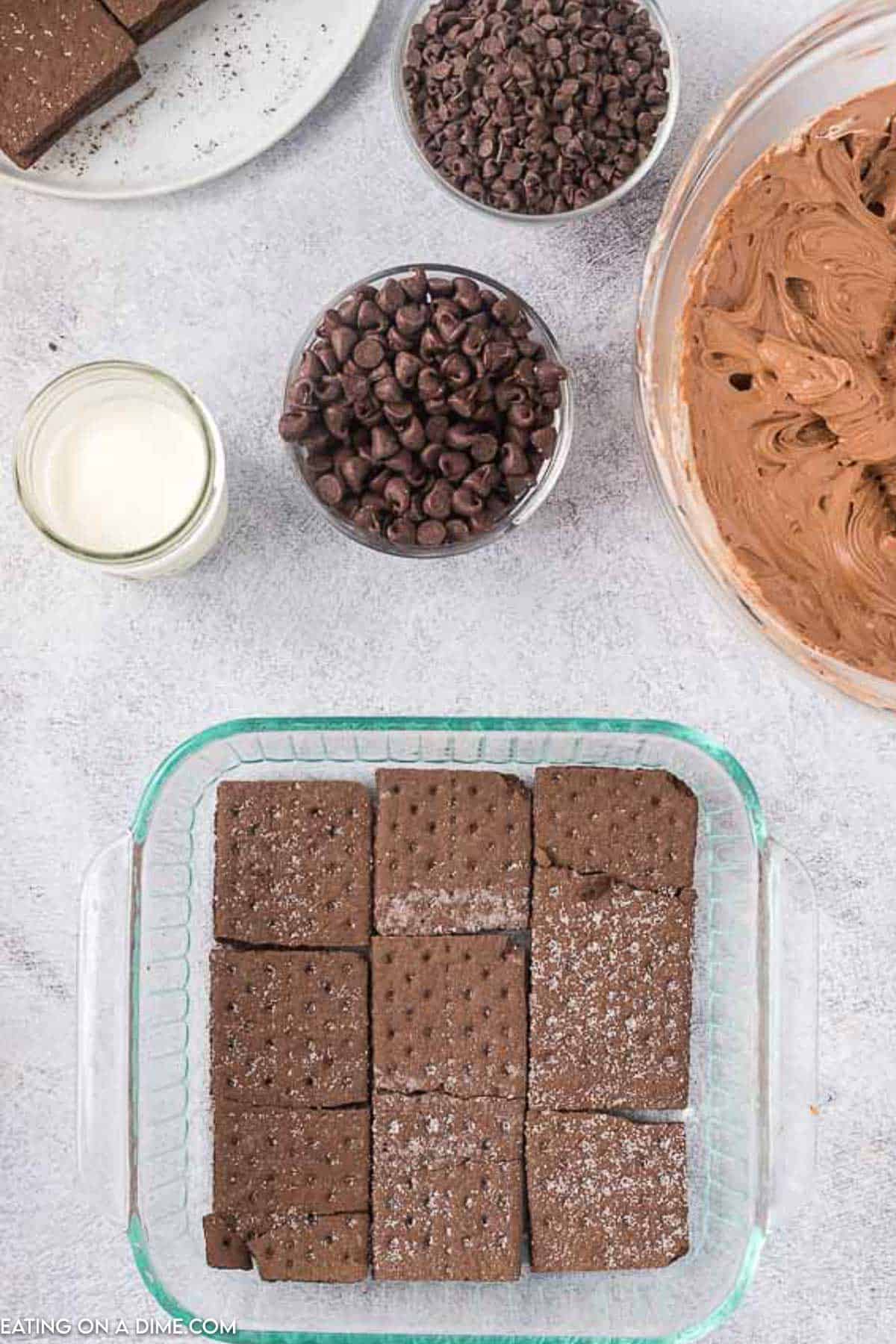 Layering the chocolate graham crackers in a baking dish with small bowls of chocolate chips on the side