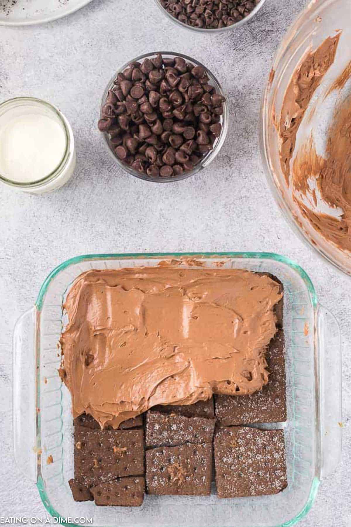 Chocolate Graham Crackers in a baking dish topped with chocolate layer on top of the crackers with small bowls of chocolate chips