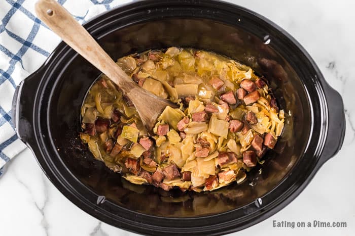 Cooked shredded cabbage and ham in a slow cooker with a wooden spoon