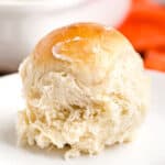 A close-up of a fluffy, golden-brown dinner roll with a shiny, buttery top, sitting on a white plate—just like the classic King's Hawaiian rolls recipe.