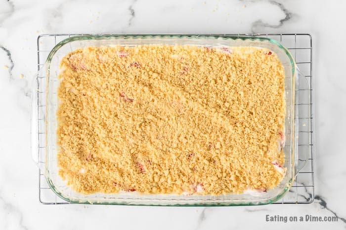 Topping the strawberry mixture with the crushed cookies to freeze