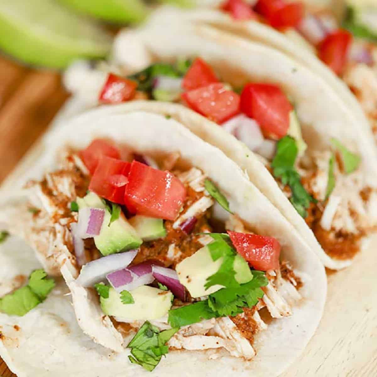 Chipotle chicken tacos on a plate topped with tomatoes, red onion, and cilantro