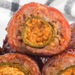 A close-up of Armadillo Eggs—sliced meat rolls stuffed with a cheese and jalapeño filling, revealing the creamy orange center and green pepper ring nestled inside the cooked, seasoned meat exterior.