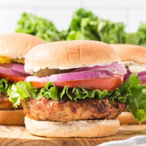 Three chicken burgers with lettuce, tomatoes and onions.
