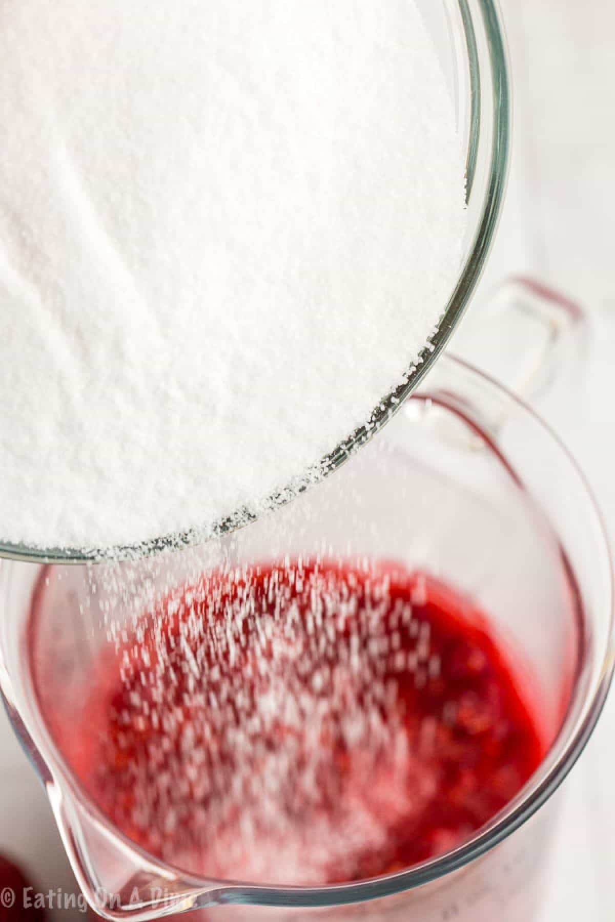 Pouring in the sugar into the mashed raspberries