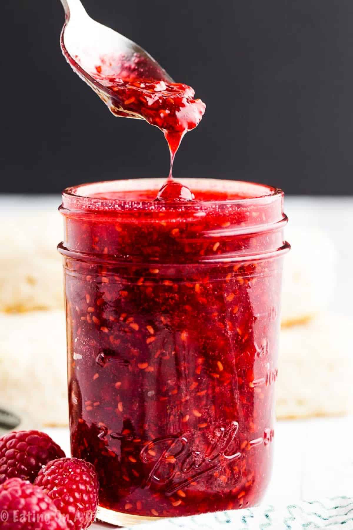 Raspberry Jam in a mason jar with a serving on a spoon