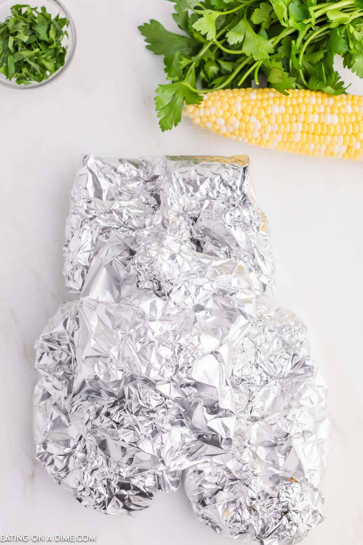 Folding the foil around the food with a corn on the cob on the side