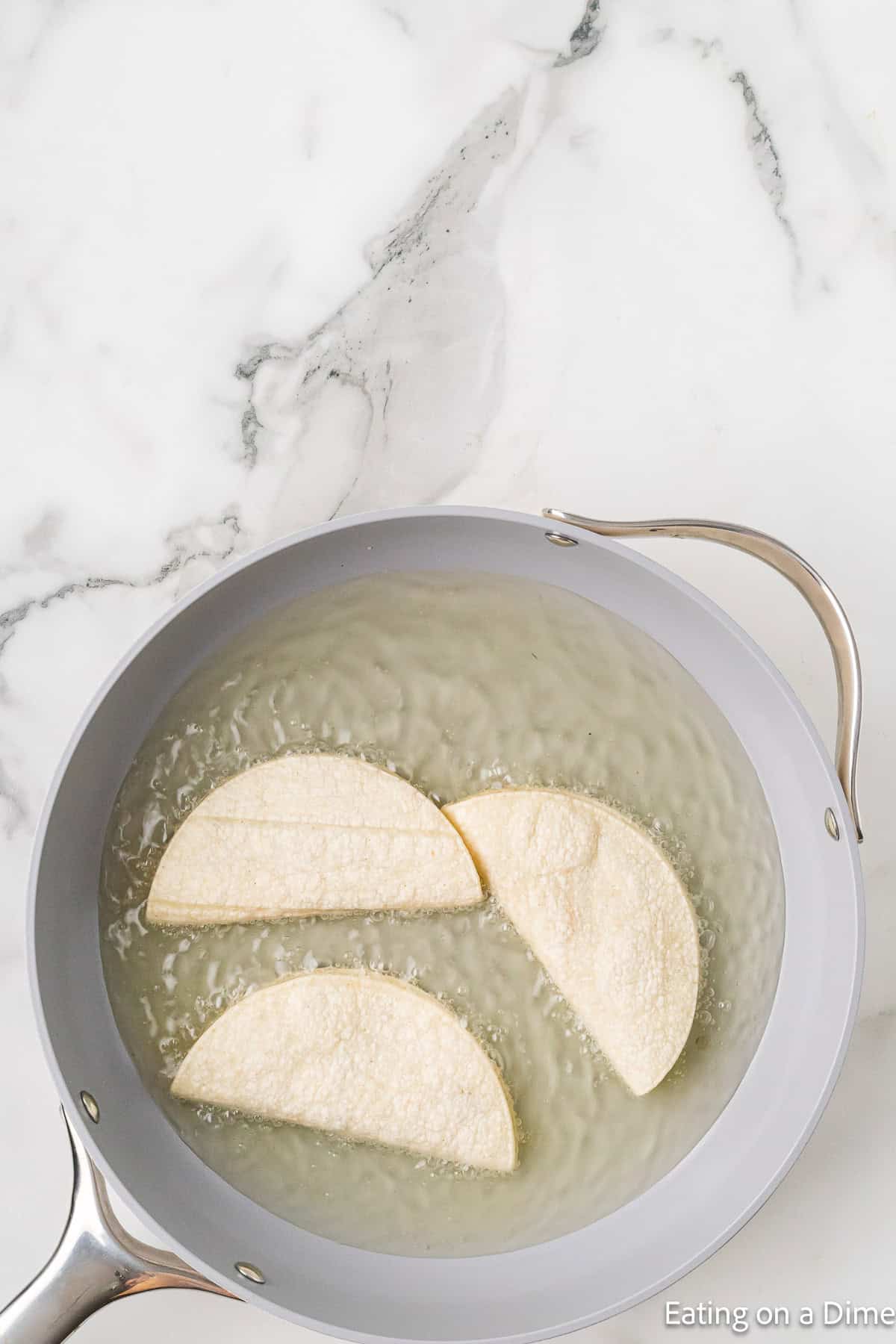 Placing corn tacos in a skillet with oil