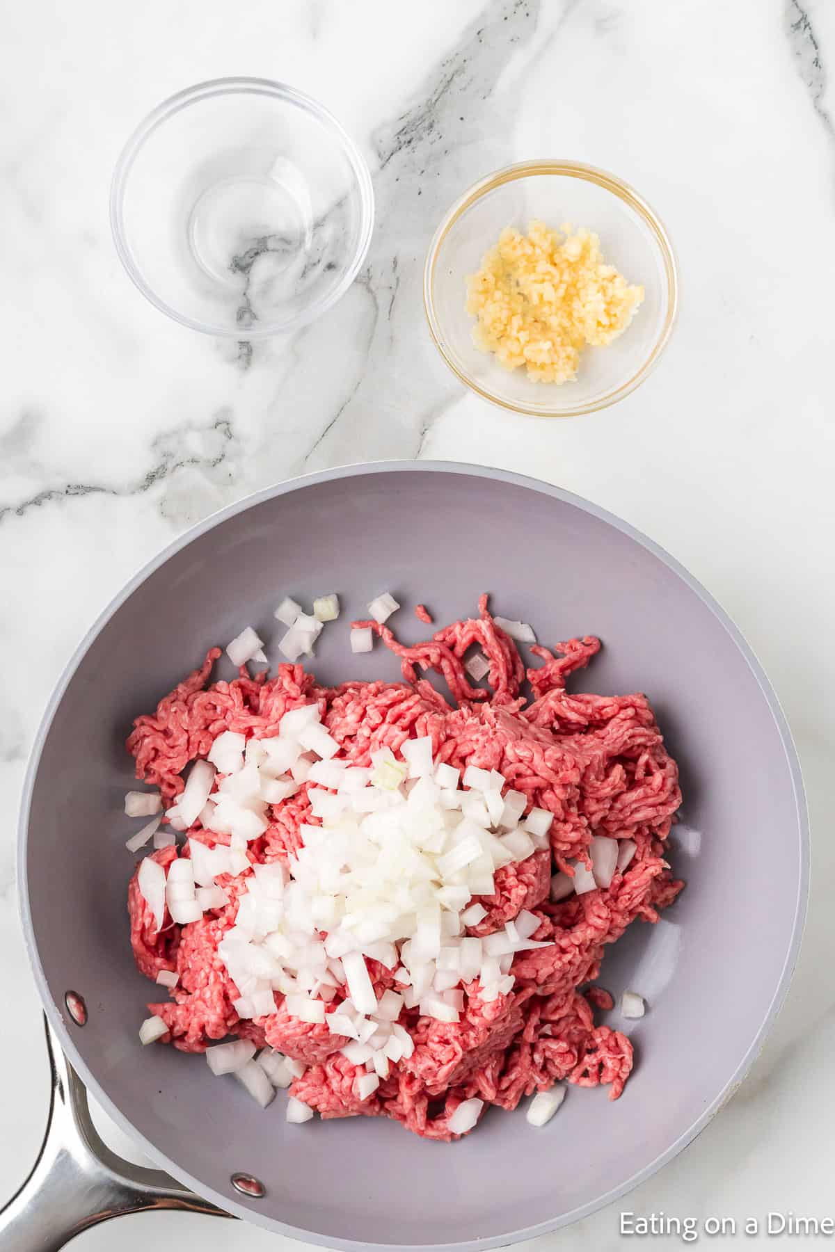 Cooking ground beef in a skillet topped with chopped onions