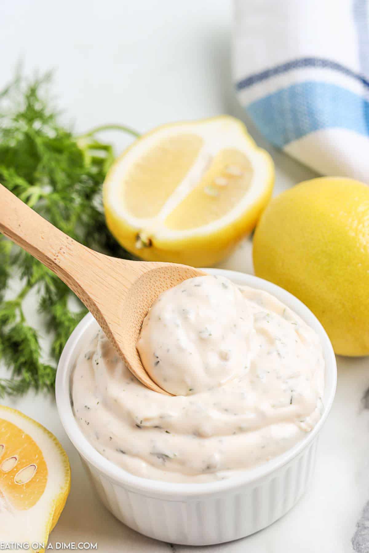 A large wooden spoonful of tartar sauce being dipped out of a small white bowl. 