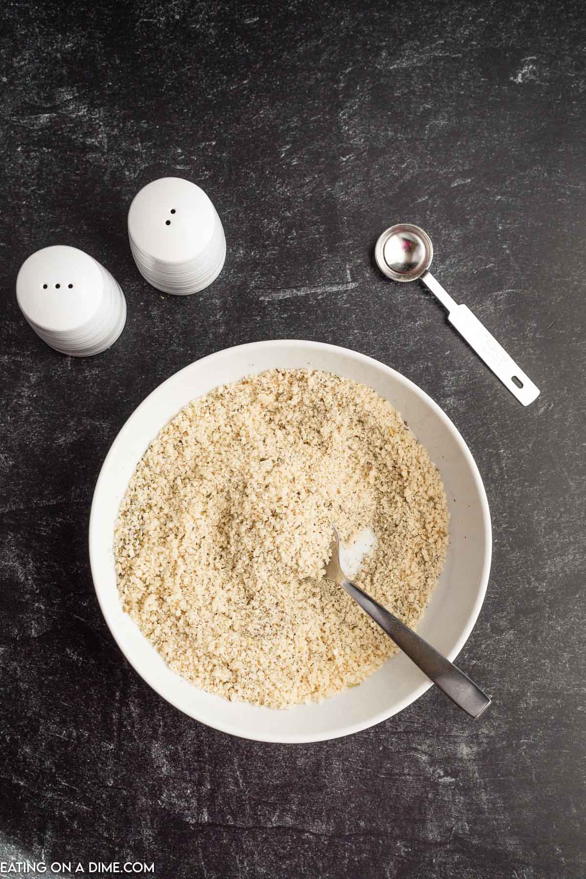 Combining the bread crumbs and seasoning in a bowl with salt and pepper shakers on the side