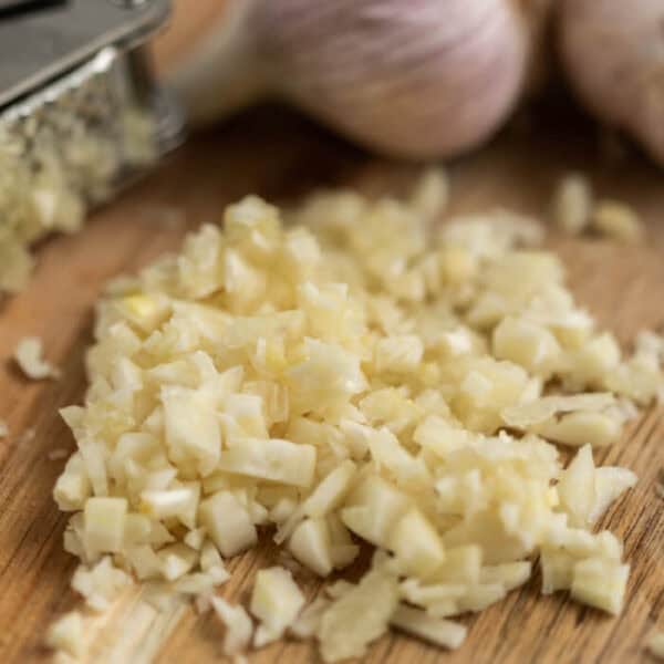Finely chopped garlic on a wooden cutting board, with whole garlic bulbs and a metal grater in the backgroundโperfect when searching for the best garlic substitute for your favorite recipes.