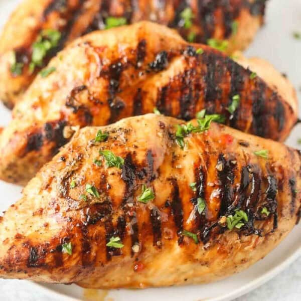 3 grilled chicken breasts on a white plate topped with fresh chopped parsely.