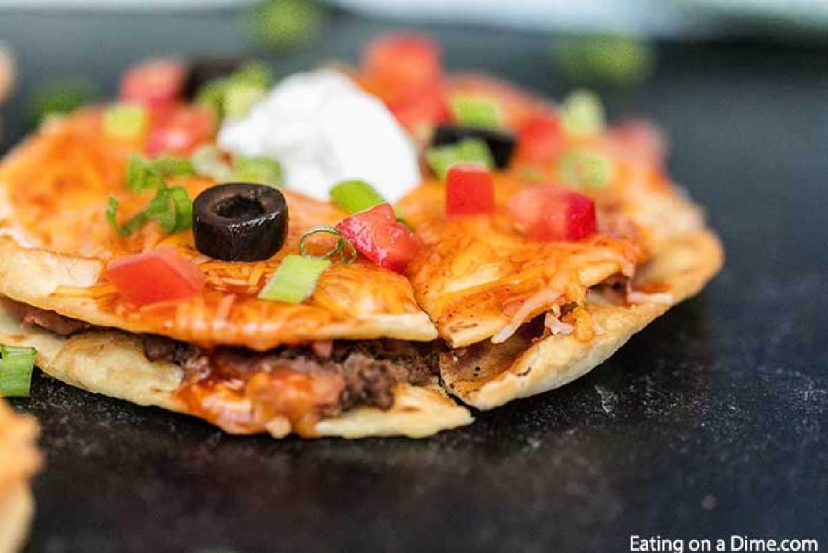 Mexican Pizza topped with black olives, diced tomatoes, sour cream and chopped green onions