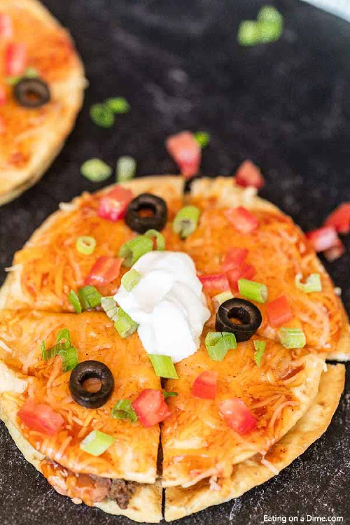 Mexican Pizza topped with sour cream, chopped green onions and slice black olives