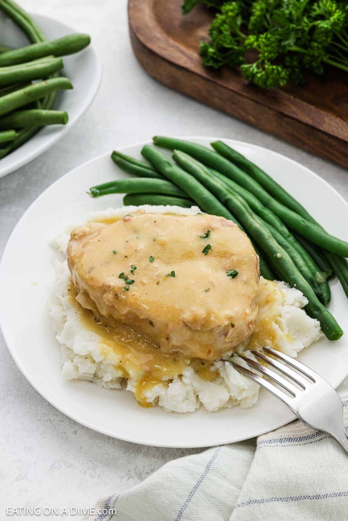 Cooked pork chops and gravy over mashed potatoes with a side of fresh green beans.