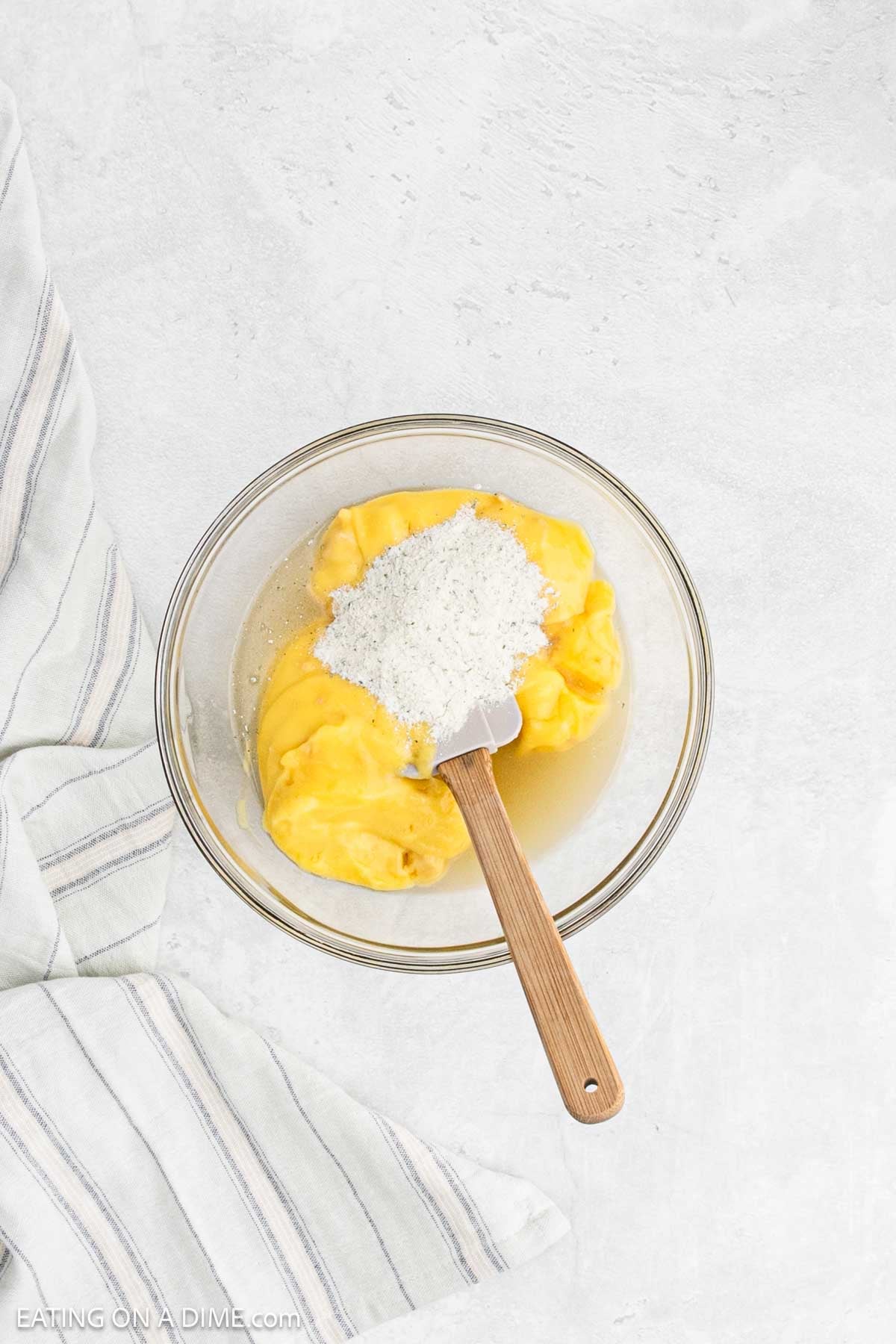Combining cream of chicken soup, ranch seasoning mix, and chicken broth in a bowl with a spatula.