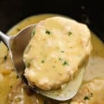 A serving of pork chops with gravy on a spatula with the rest of the cooked pork chops in the slow cooker.