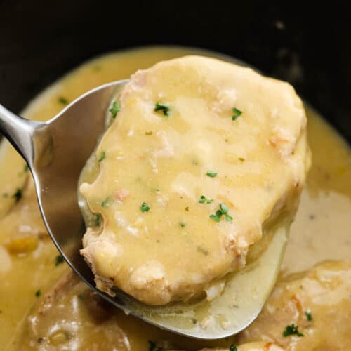 A serving of pork chops with gravy on a spatula with the rest of the cooked pork chops in the slow cooker.