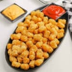 Air Fryer Tator Tots on a white platter with a bowl of ketchup on the side.