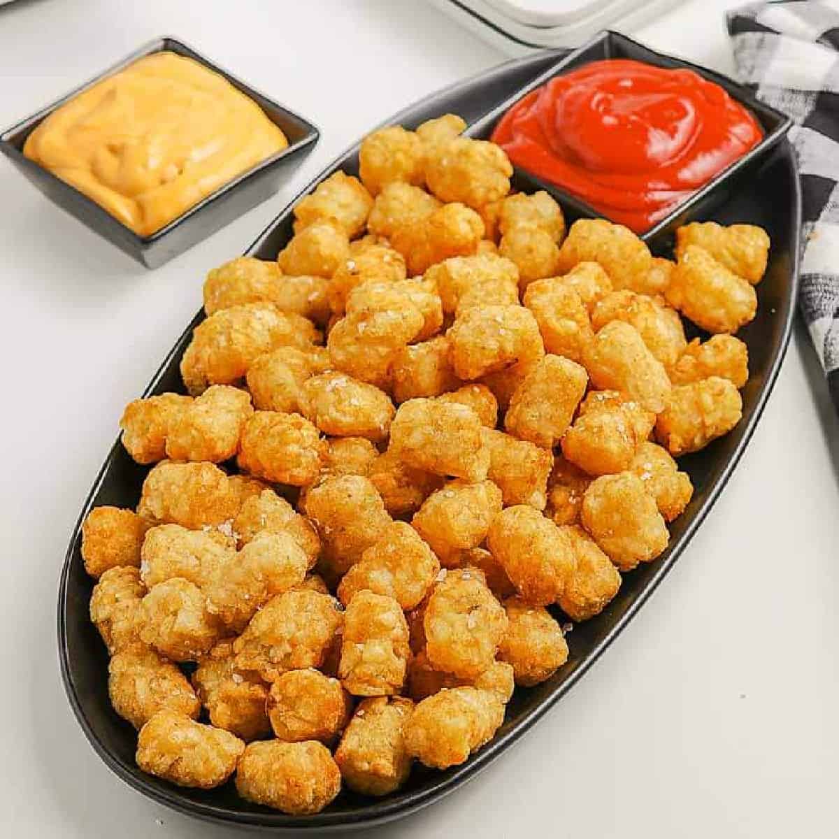 Air Fryer Tator Tots on a white platter with a bowl of ketchup on the side.