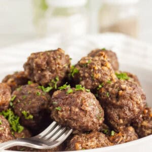 Meatballs stacked in a bowl with a fork piercing one of the meatballs.