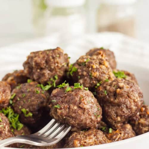 Meatballs stacked in a bowl with a fork piercing one of the meatballs.