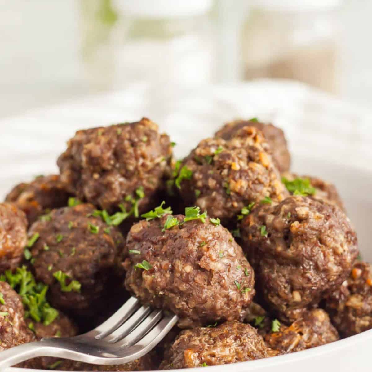 Meatballs stacked in a bowl with a fork piercing one of the meatballs.