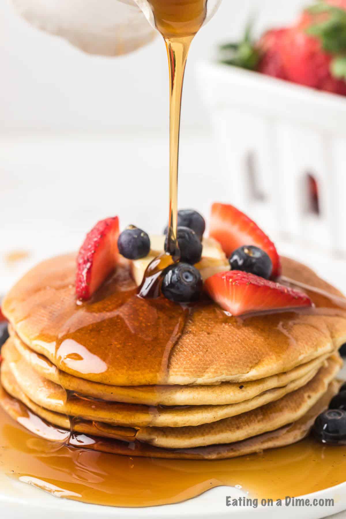 Gluten free pancakes recipe is so light and fluffy that even your gluten loving friends will want this recipe. Try this tasty pancake recipe. Gluten Free pancakes stacked on a plate with syrup being poured over the top with fresh blueberries and strawberries