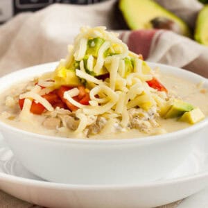 A bowl of chicken tortilla soup topped with diced avocado, tomatoes, shredded cheese, and green onions.
