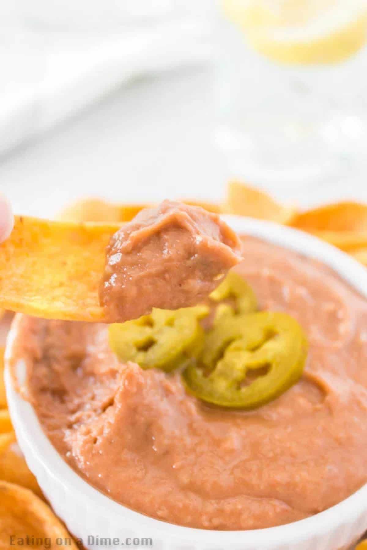 Bean dip in a bowl topped with slice Jalapenos with a serving on Fritos